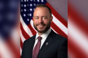 Tustin Mayor Austin Lumbard in a suit and City of Tustin lapel pin, smiling in front of an American flag
